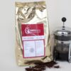 kilo kaffee goldener alubeutel rot-weisses Etikett stempelkanne mit Kaffee drinnen und geröstete Bohnen vorne ausgebreitet