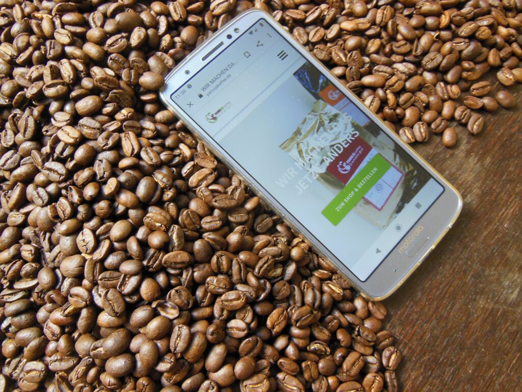 dunkelbrauner Tisch Kaffeebohnen Handy Photo zeigt Pamoja Website Slogan Wir machen das jetzt anders