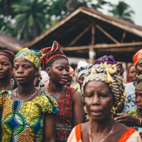 Privates Engagement als Problemlöser hilft Dorf mit Frauen in Afrika bunte Kleider Schmuck Hintergrund Holzhaus