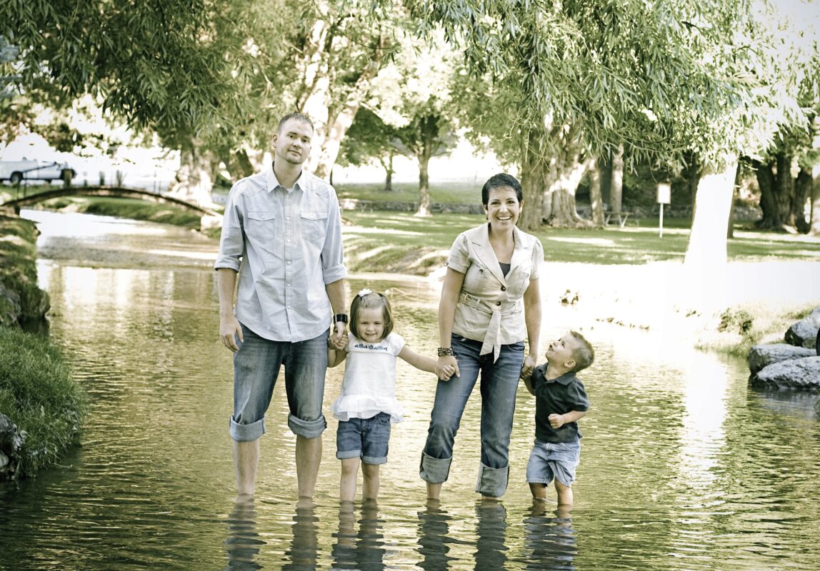 Sammelbestellung Eltern mit zwei Kindern stehen im Wasser Hosenbeine hoch Hintergrund Bäume