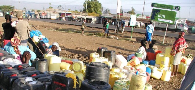 afrikanische frauen und kinder warten auf wassermit leeren gelben 20 liter kanistern warten am staubigen straßenrand